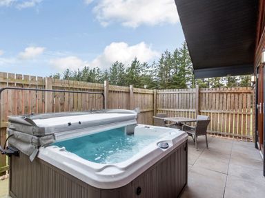 An outdoor area with a hot tub and a table with chairs at Raeburn Premier Spa (Pet) Dundee