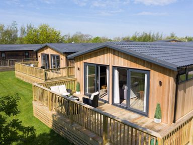 A wooden deck with chairs in front of cabins at Dovecote in Waltham