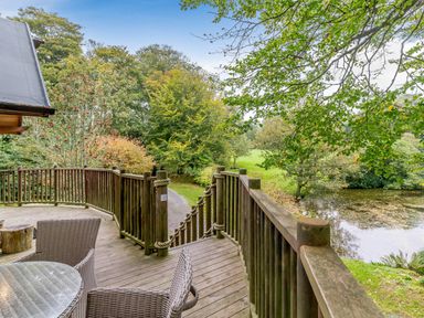 An outdoor area with a wooden deck overlooking trees and a pond at The Treehouse in Praze-An-Beeble
