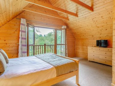 A bedroom with a bed and windows at Woodland Lodge Spa in Praze-An-Beeble