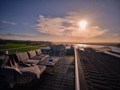 A terrace with a sofa and table overlooking a river at Sonnet 3 Roof Terrace Spa in Laugharne