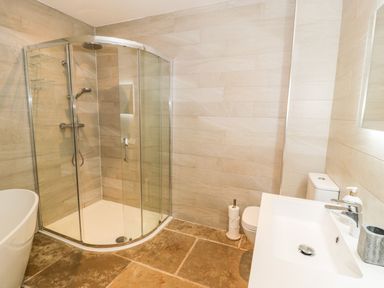 A bathroom featuring a shower, bathtub, toilet, and sink at Cae Sam in Pentraeth