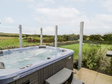 A hot tub with a view of grass and stone wall at Cae Sam in Pentraeth
