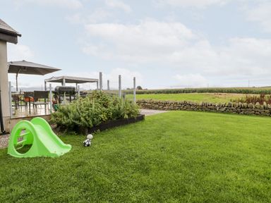 A garden with a green slide, seating area, and fenced perimeter at Cae Sam in Pentraeth