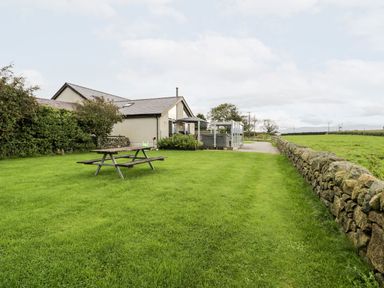 A garden with a picnic table and stone wall at Cae Sam in Pentraeth