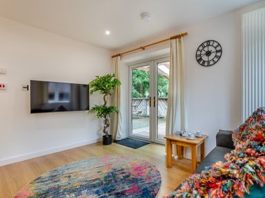 A living room with a television and doors leading to a deck at Poldark Spa Pet Perranporth