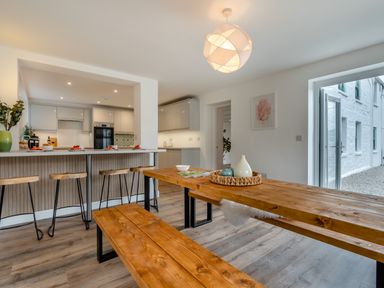 A dining room with a wooden table and kitchen view at The Farmhouse (Pet) Perranporth