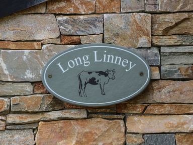 A sign with the name Long Linney and a cow illustration on a stone wall at Long Linney in Bideford