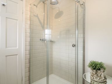 A shower with glass doors and tiled wall at Ostlers in Burford