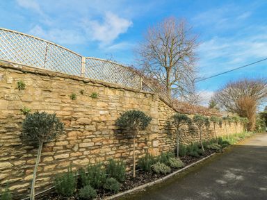 A garden with a stone wall and trees at Ostlers in Burford