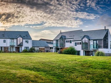 A view of houses with grass and cloudy sky at Chapel Park in Marhamchurch