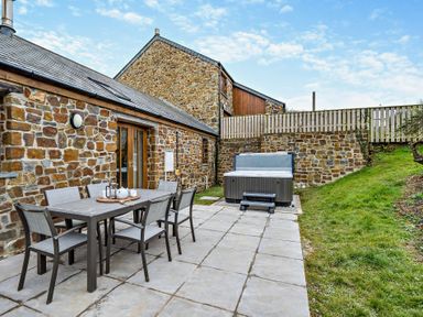 An outdoor patio with a table and chairs next to a hot tub at Long Down Spa in Marhamchurch