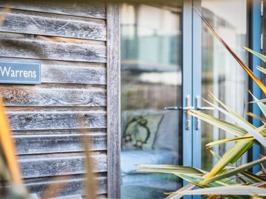 A wooden wall with a sign and glass door at Warrens Spa in Marhamchurch
