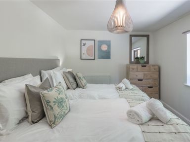 A bedroom with two beds, a chest of drawers, and wall art at Windy Hills Spa in Marhamchurch