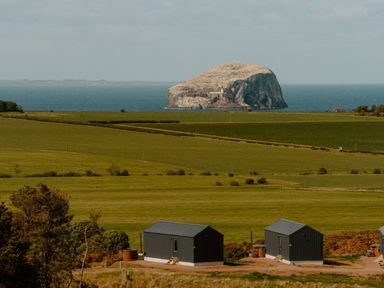 A view of a rock formation by the sea with huts on grassland at The Telfer in North Berwick