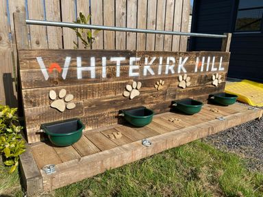 A wooden dog station with bowls and paw prints at Whitekirk Hill North Berwick