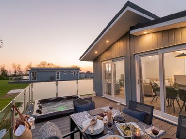 An outdoor deck with a hot tub and dining setup at Mullion 2 Spa (Pet) Bude