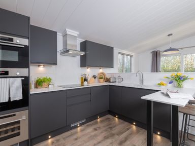 A kitchen with dark cabinets and stainless steel appliances at Mullion 2 Spa (Pet) Bude
