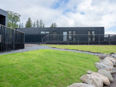 A black building with a wooden railing and grass at Cabin 2.0 Deluxe in Dumfries