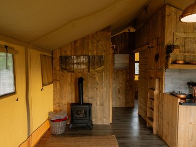 A tent interior with a wood stove and shelves at Deluxe Safari Tent in Fair Oak