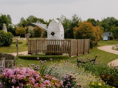 A garden with a windmill and flowerbeds at Spitfire Lodge in Fair Oak
