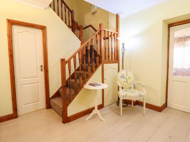 A hallway with a staircase and chair at Llwyn Derw in Talybont