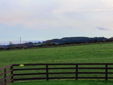 A field with a wooden fence and distant hills at Rosefinch Cabin in Scarborough