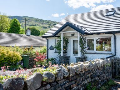 A cottage with a stone wall and flowers outside at Oaks Lodge Cottage Ambleside