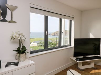 A living room with a television and a window showing a sea view at Praa Waves in Penzance