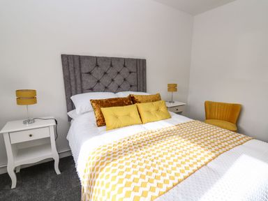 A bedroom with a bed, bedside tables, and a chair at Tymelyn in Aberystwyth