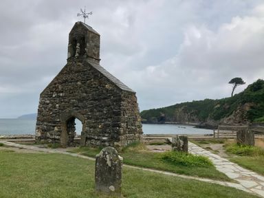 A stone church near water with a pathway and bench at Caravan 38 Newport
