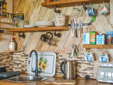 A kitchen with a sink and shelves containing cups and plates at The Retreat Cabin Llanelli