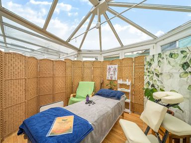 A conservatory with a massage setup and folding screens at The Retreat Cabin in Llanelli