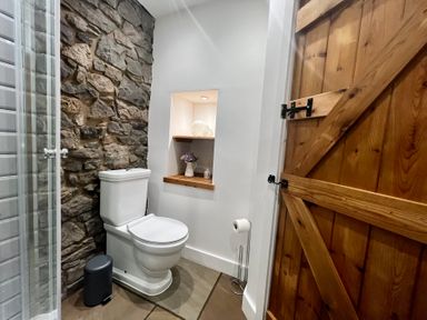 A bathroom with a toilet and stone wall at Penderyn Cottage in Aberdare