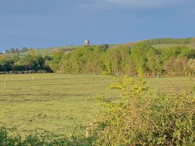 A field with trees and a water tower on a hill at Cosy Escape in Sheerness