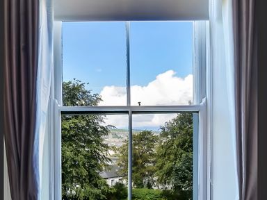 A window with curtains showing trees and sky at Fountain Hill House Londonderry