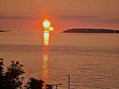 A sunset over the water with an island at Sea view cottage in Penmaenmawr