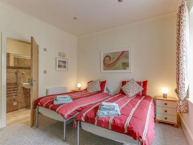 A bedroom with two beds and a bathroom door at Poppyfields Stable in Redruth