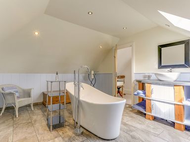 A bathroom with a bathtub, sink and mirror at Poppyfields Stable in Redruth