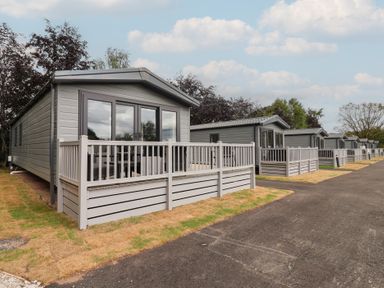 A row of cabins with decking and grass area at The Pines 3 Bedrooms Delamere