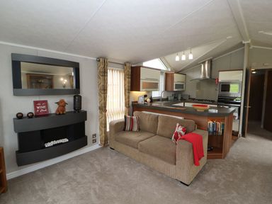 A living room with a sofa and kitchen area at No 8 Hillcote Lodge in Cockermouth