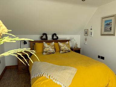 A bedroom with a yellow bedspread and nightstand at Lowenna Watergate Bay near Newquay