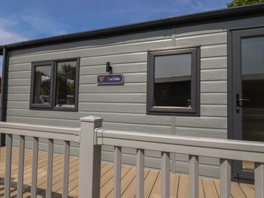 An exterior view of The Oaks cabin with windows and decking in Delamere
