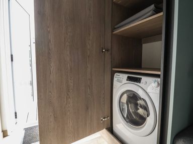 A washing machine inside a wooden cabinet at Cedar Lodge 2 Bedrooms with hot tub Delamere