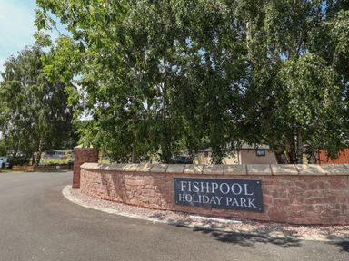 A sign for Fishpool Holiday Park surrounded by trees in Delamere