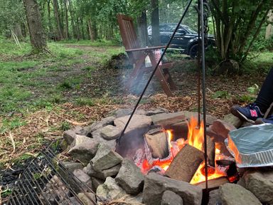 A fire pit with burning wood and a grill at The Tree House in the Woods Longhope