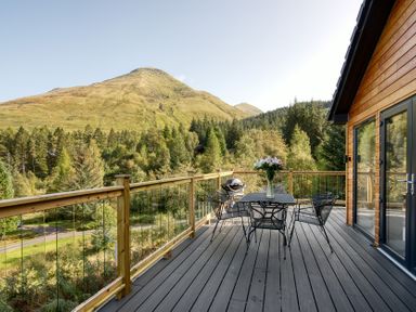 An outdoor deck with a table and chairs overlooking mountains at Pinemarten Lodge Crianlarich