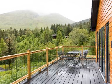 An outdoor area with a table and chairs on a deck at Pinemarten Lodge Crianlarich