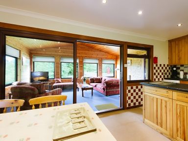 A kitchen with a table and chairs and a view to a living area at Buzzard Lodge in Crianlarich