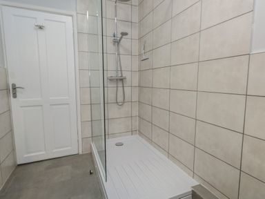 A shower area with tiled walls and a door at Tudor Rose in Weymouth
